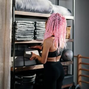 A yoga instructor with pink braids arranges equipment in an indoor studio, promoting wellness and fitness.